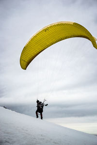 Low angle view of man paragliding on snowcapped mountain against cloudy sky