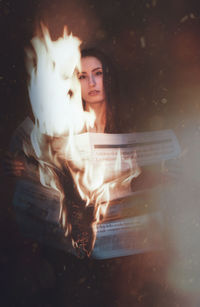 Portrait of young woman holding burning newspapers