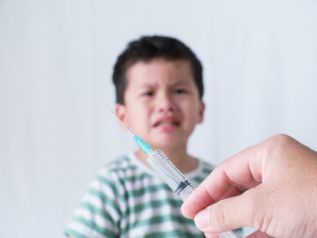 Close-up of doctor holding syringe with crying boy in background