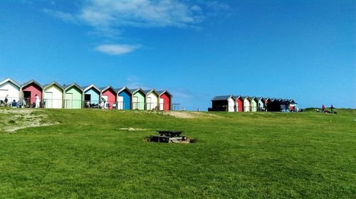 Beach huts on grassy shore against blue sky