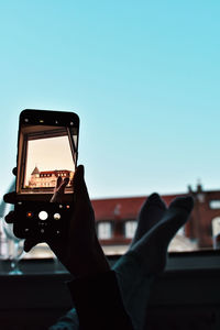 Low section of person photographing smart phone against sky