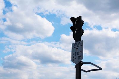 Low angle view of road signal with text against cloudy sky