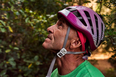 Closeup of senior male climber wearing safety helmet looking down while standing against cliff