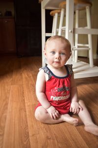 Portrait of cute baby girl sitting on hardwood floor