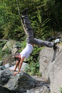 Portrait of smiling mature woman doing handstand on rocks