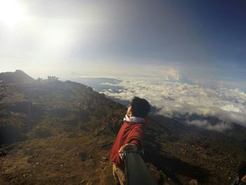 Man taking selfie while standing on mountain against cloudy sky