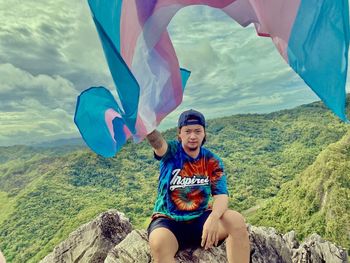 Portrait of smiling young man sitting on mountain against sky