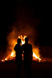 Rear view of silhouette couple standing by bonfire at night