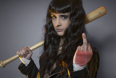 Portrait of young female model holding baseball bat against gray background