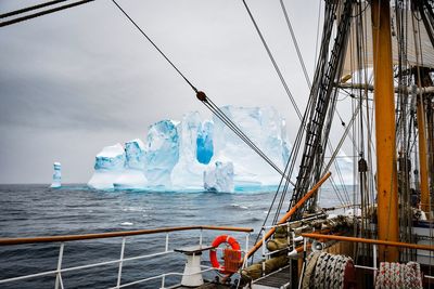 Tall ship by iceberg in sea against sky