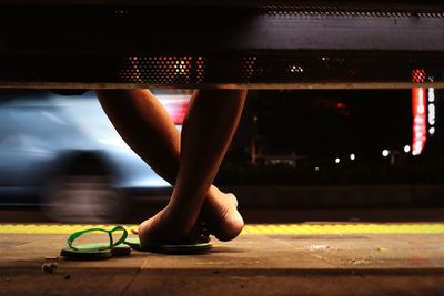 Low section of woman sitting on seat at roadside during night