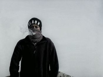 Portrait of man smoking through scarf against clear sky