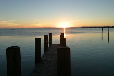 Wooden posts in sea against sky during sunset