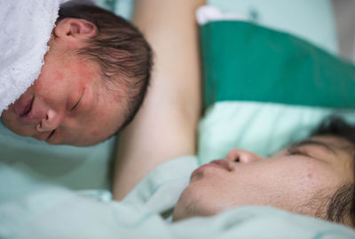 Close-up of baby boy sleeping by mother on bed in hospital