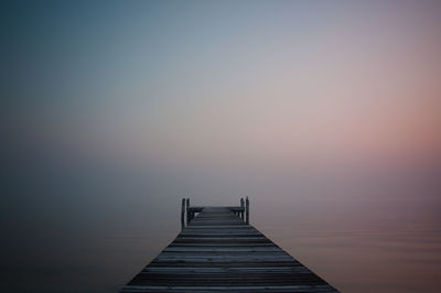 Pier over sea against clear sky at sunset