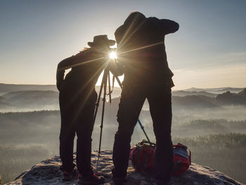 Two hikers take pictures and talk on top of mountain. photographers with photo gear relaxing on top