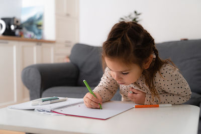 Portrait of cute preschooler child girl drawing with pencils at home while sitting in front 