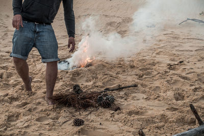 Low section of man by bonfire at sandy beach