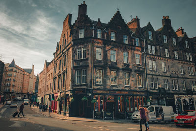 People walking on road amidst buildings in city against sky