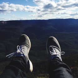 Low section of man relaxing against mountains and cloudy sky during sunny day