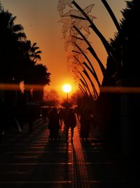 Silhouette people walking on illuminated street against orange sky