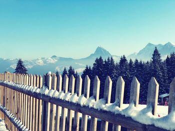 Fence on snowcapped mountains against clear blue sky