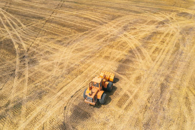 Orange tractor driving through the mown wheat field. farmers at work. agriculture harvesting season.