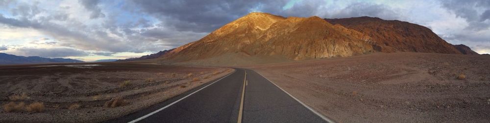 Road leading towards mountains against cloudy sky