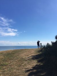 Rear view of man standing on shore against sky