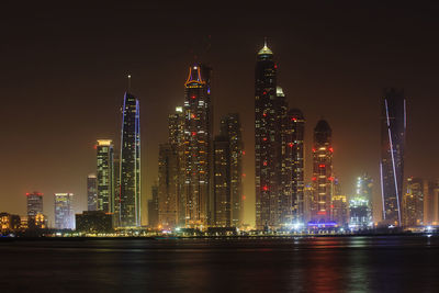 Sea against illuminated princess tower and cayan tower amidst city
