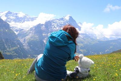 Rear view of woman sitting with stuffed toy against mountain range