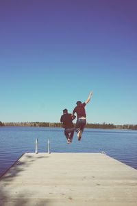 Friends diving into lake against sky