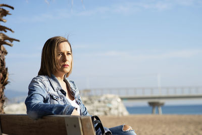 Thoughtful woman sitting on a bench near sea while looking away