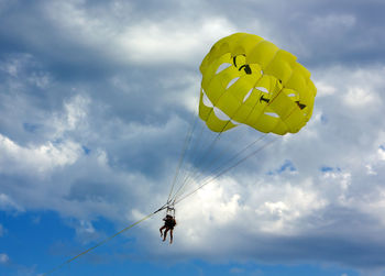 Low angle view of people paragliding against sky