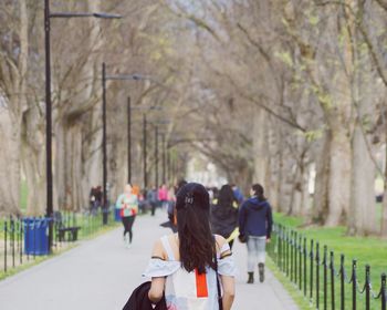 Rear view of people walking on bare trees