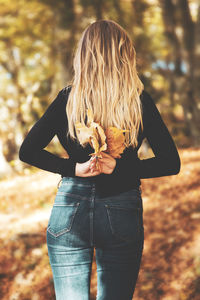 Rear view of woman holding autumn leaf standing against tree