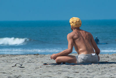 Rear view of shirtless man sitting on beach