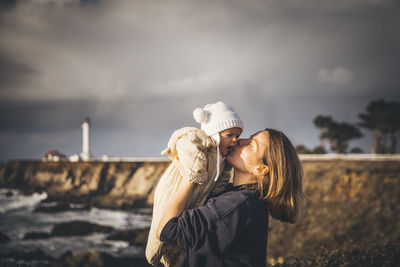 A woman is holding a baby near a lighthouse on the pacific coast