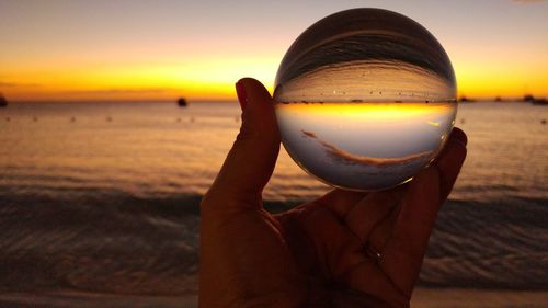 Close-up of hand holding crystal ball with sea reflection at sunset