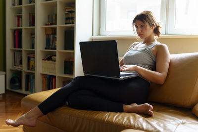 Young woman using phone while sitting on sofa at home