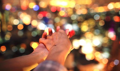 Cropped image of man holding woman hand against defocused lights