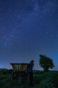 Side view of man standing by cart on land against sky at night