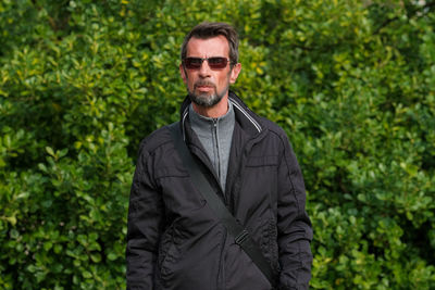 Portrait of man wearing sunglasses standing against plants