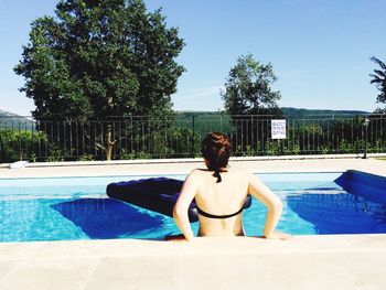 Rear view of woman in swimming pool against sky on sunny day