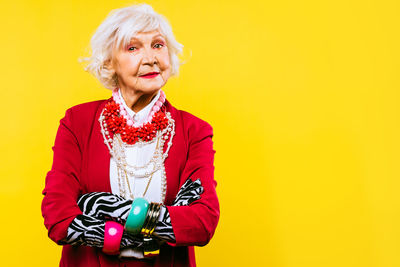 Portrait of senior woman standing against yellow background