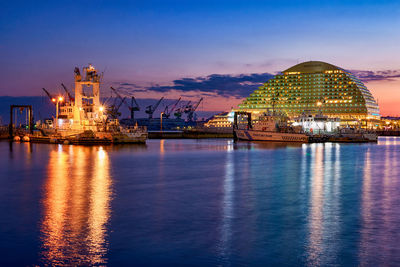 Illuminated city at waterfront during sunset