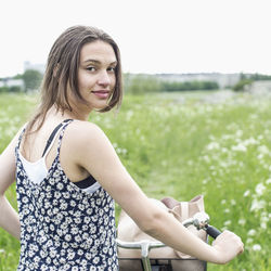 Rear view portrait of young woman with bicycle standing at field