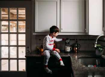 Young boy sitting on kitchen counter learning to use coffee maker