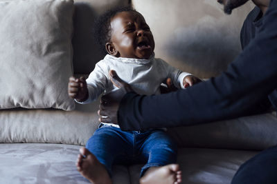 Father lifting crying baby daughter on sofa in living room