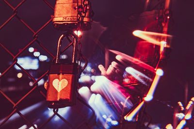 Close-up of lock hanging on chainlink fence against illuminated lights at night